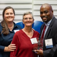 Quincy Williams poses with two women in front of GVSU logo sign